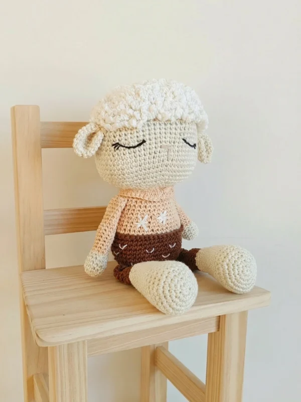 Oveja de crochet sentada en una silla de madera clara, decoración de habitación infantil estilo nórdico y minimalista.