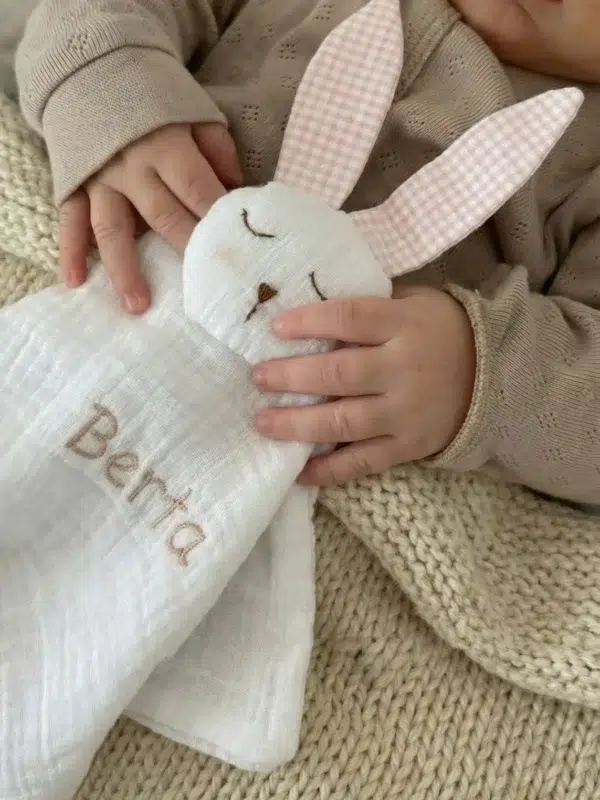 Bebé abrazando un conejito de apego blanco personalizado con el nombre Berta bordado.
