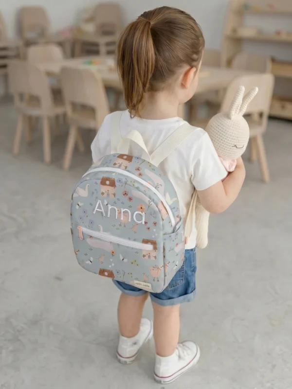 Niña con mochila infantil impermeable personalizada Jardín para guardería sosteniendo un conejito de ganchillo