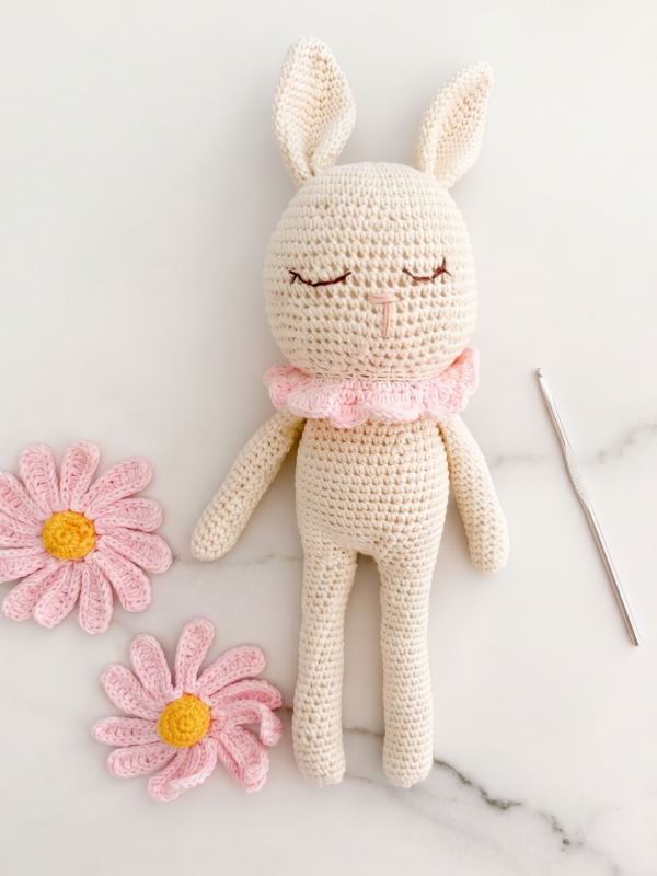 Conejito de apego para bebé tejido a mano en crochet, acompañado de flores rosas y elaborado artesanalmente.