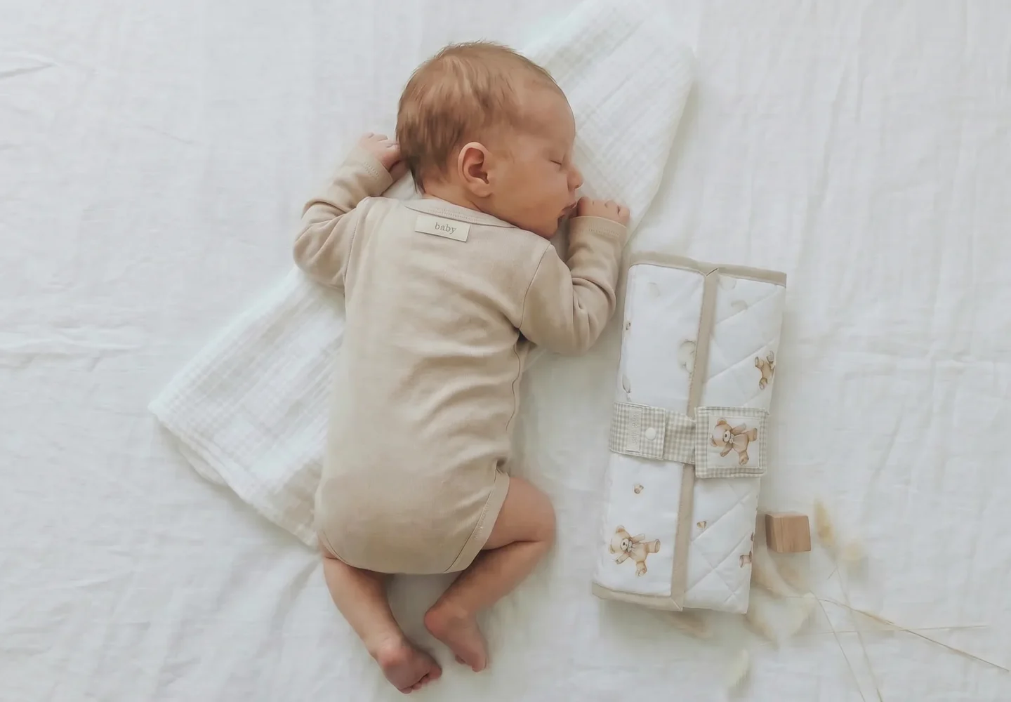 Bebé recién nacido durmiendo junto a un cambiador portátil impermeable acolchado hecho a mano de Petit Miu, ideal para cambiar al bebé fuera de casa.