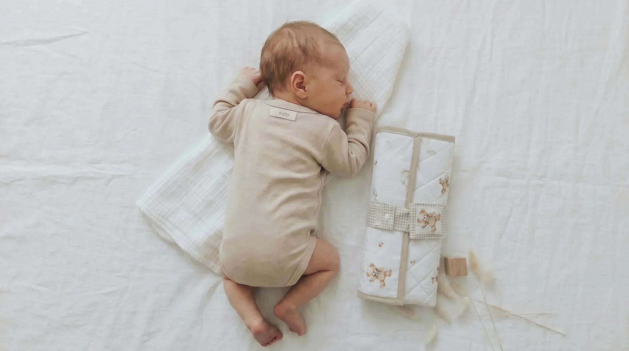Bebé recién nacido durmiendo junto a un cambiador portátil impermeable acolchado hecho a mano de Petit Miu, ideal para cambiar al bebé fuera de casa.