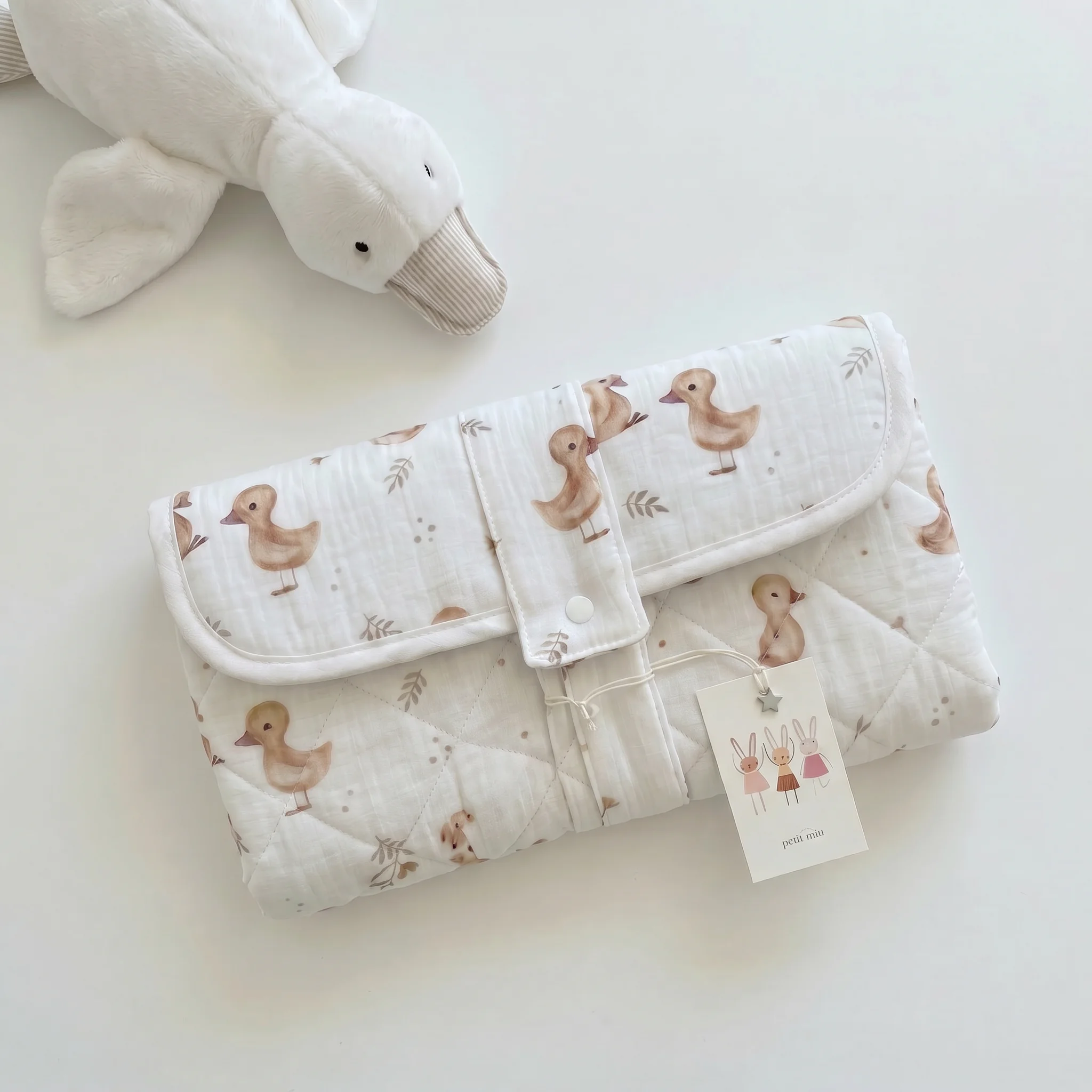Cambiador portátil impermeable con diseño de patitos en tonos beige y blanco, acompañado de un peluche duck, regalo de Petit Miu Bebé. Cambiador portátil impermeable con diseño de patitos en tonos beige y blanco, acompañado de un peluche duck, regalo de Petit Miu Bebé.