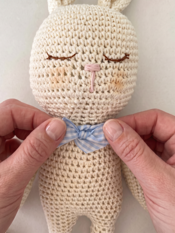Detalle de un conejito de apego para bebé tejido a mano en crochet con un pequeño lazo azul, elaborado artesanalmente.